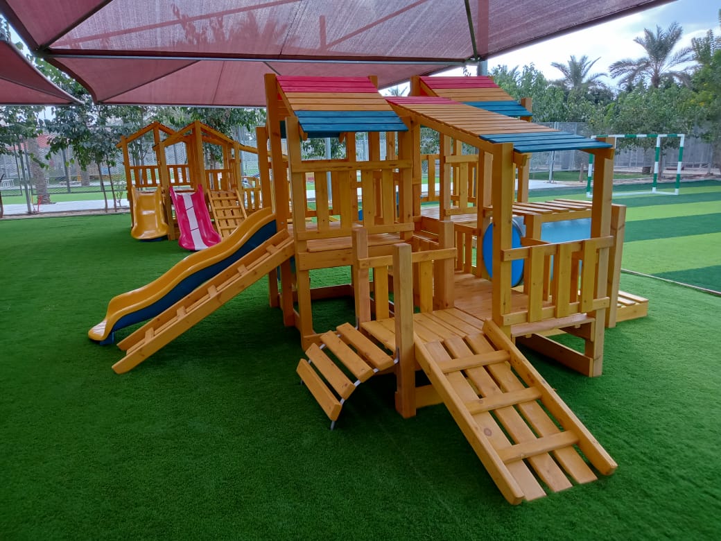 مجمع ألعاب خشبية ملون للحدائق يضم زحاليق فيبر جلاس وهياكل تسلق متينة، مثبت على نجيل صناعي مع مظلة علوية للحماية من الشمس، يوفر بيئة ترفيهية آمنة ومبهجة للأطفال.